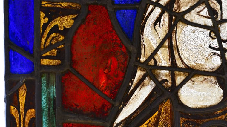 Portion of a stained glass window, blue, red and yellow glass, a women's face, hair, shoulder and gold gown.